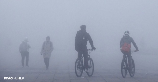 En la imagen se observan dos ciclistas que pedalean en medio de la niebla y dos personas caminando, todas bien abrigadas.